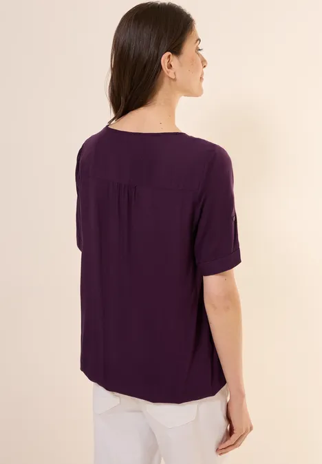 Frau mit lila Bluse und weißen Hosen von hinten.
